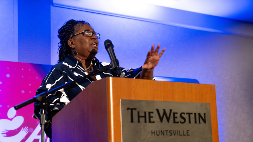 A speaker gesturing while addressing the audience from The Westin Huntsville podium